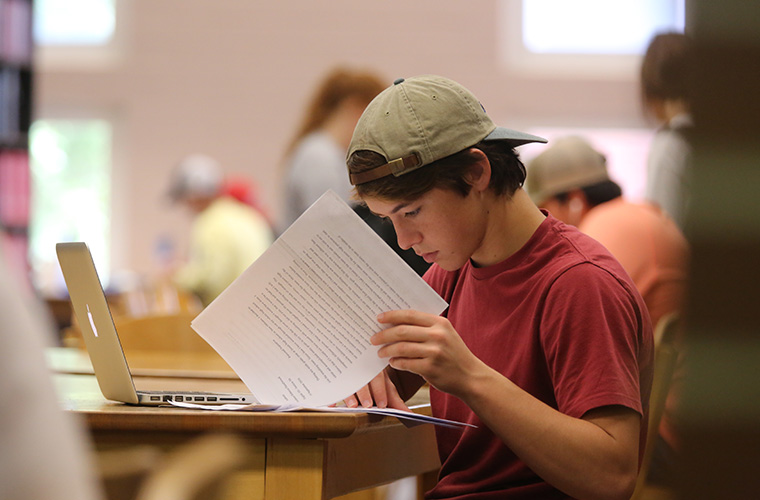 UL Lafayette student reviewing printed paper at University library.