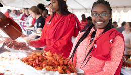 UL Lafayette student in a red pullover holding a tray of crawfish at Lagniappe Day