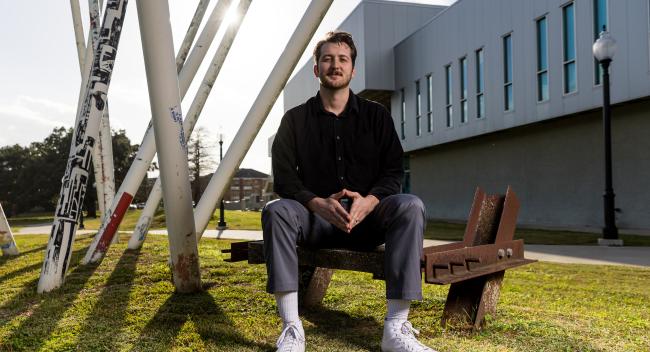 Professional photo of Christian Willis sitting down in front of the university's architecture.