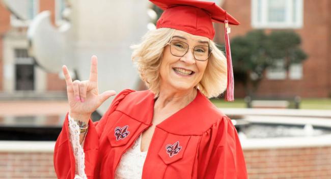 Cheri Landry Vallery smiles and poses for a photo in her cap and gown on UL Lafayette's campus.