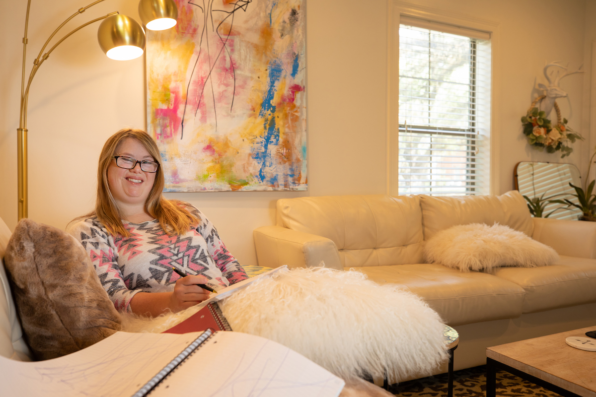 UL Life student Alex Mack smiles on a white couch with a notebook in her hands