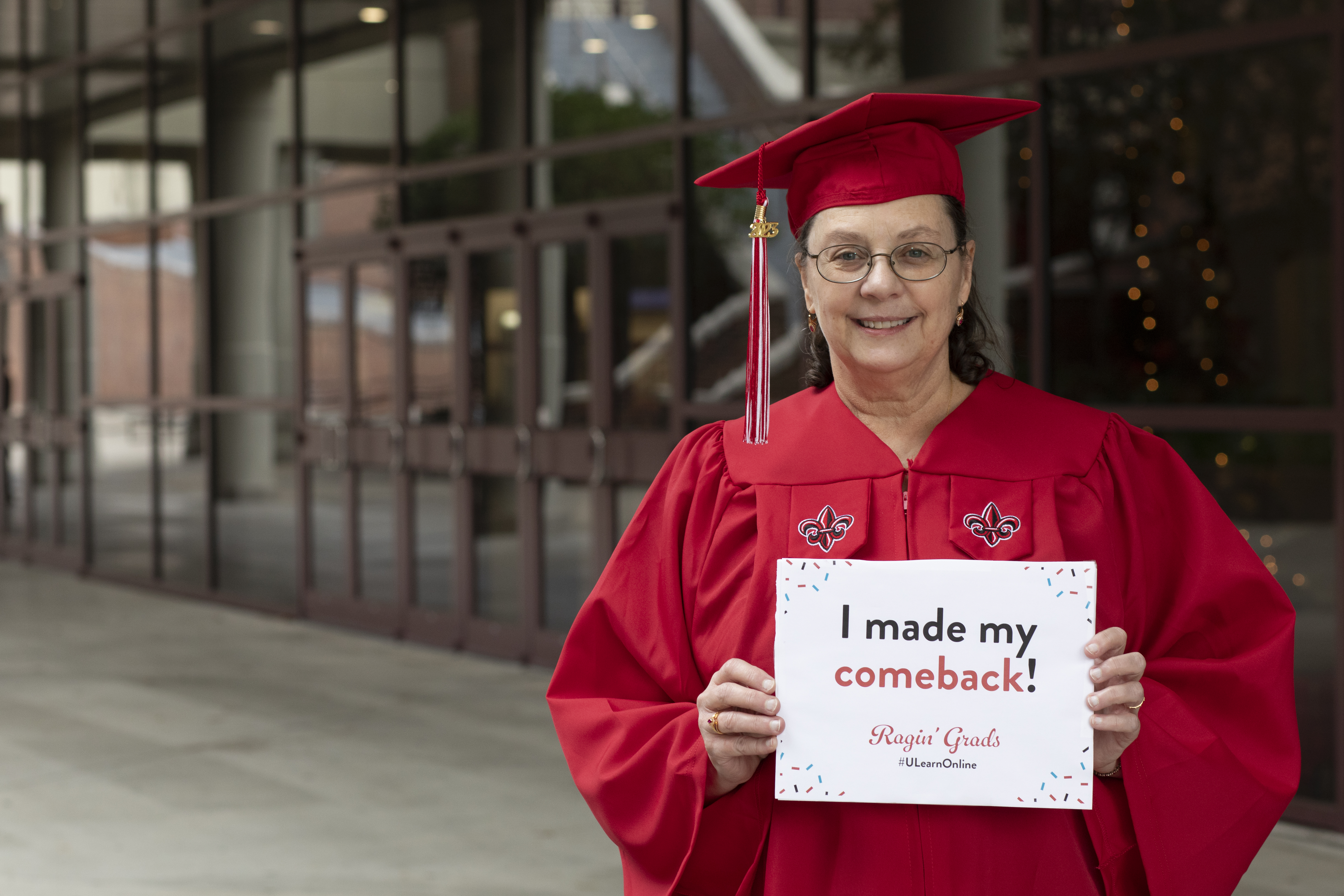 Karen LeDoux, wearing her cap and gown, holds up a sign that reads, "I made my comeback!"