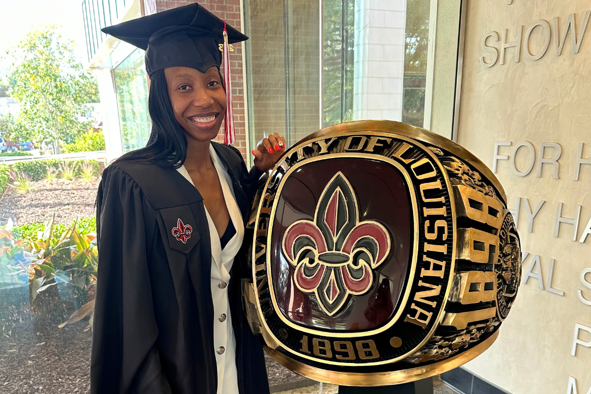 Wearing her cap and gown, April Piper stands next to a large replica of UL Lafayette's class ring.