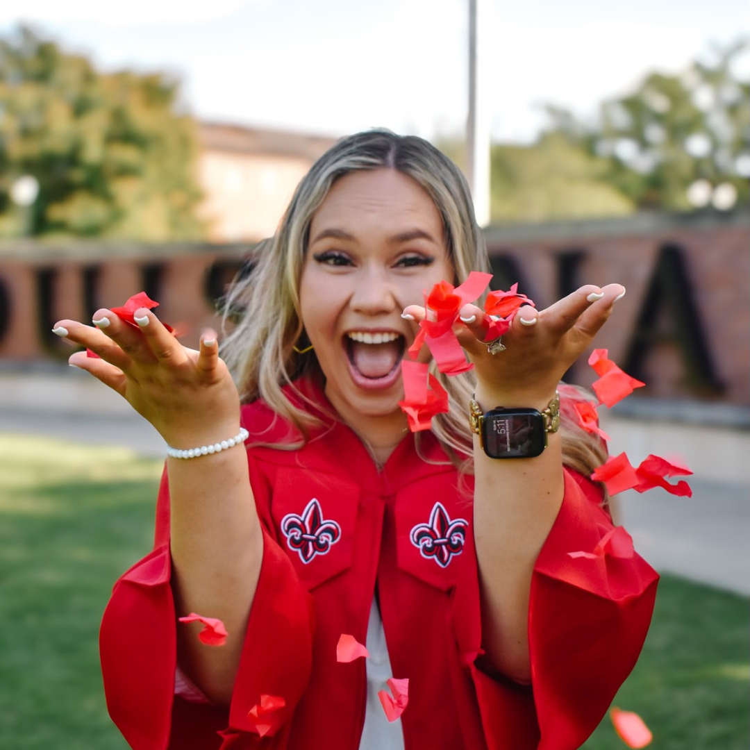 Online general studies grad throwing up red confetti, dressed in her red UL Lafayette graduation gown.