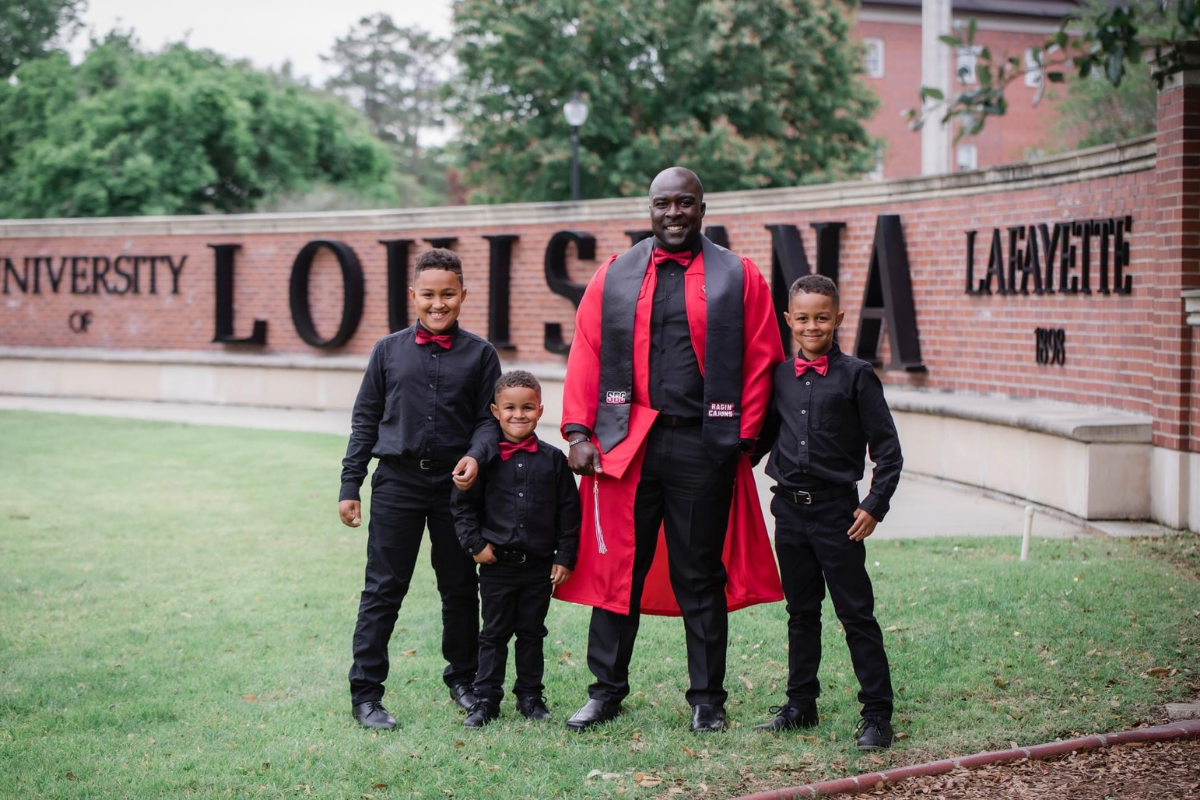 General Studies graduate and his 3 sons smile in front of the University of Louisiana at Lafayette sign in formal attire