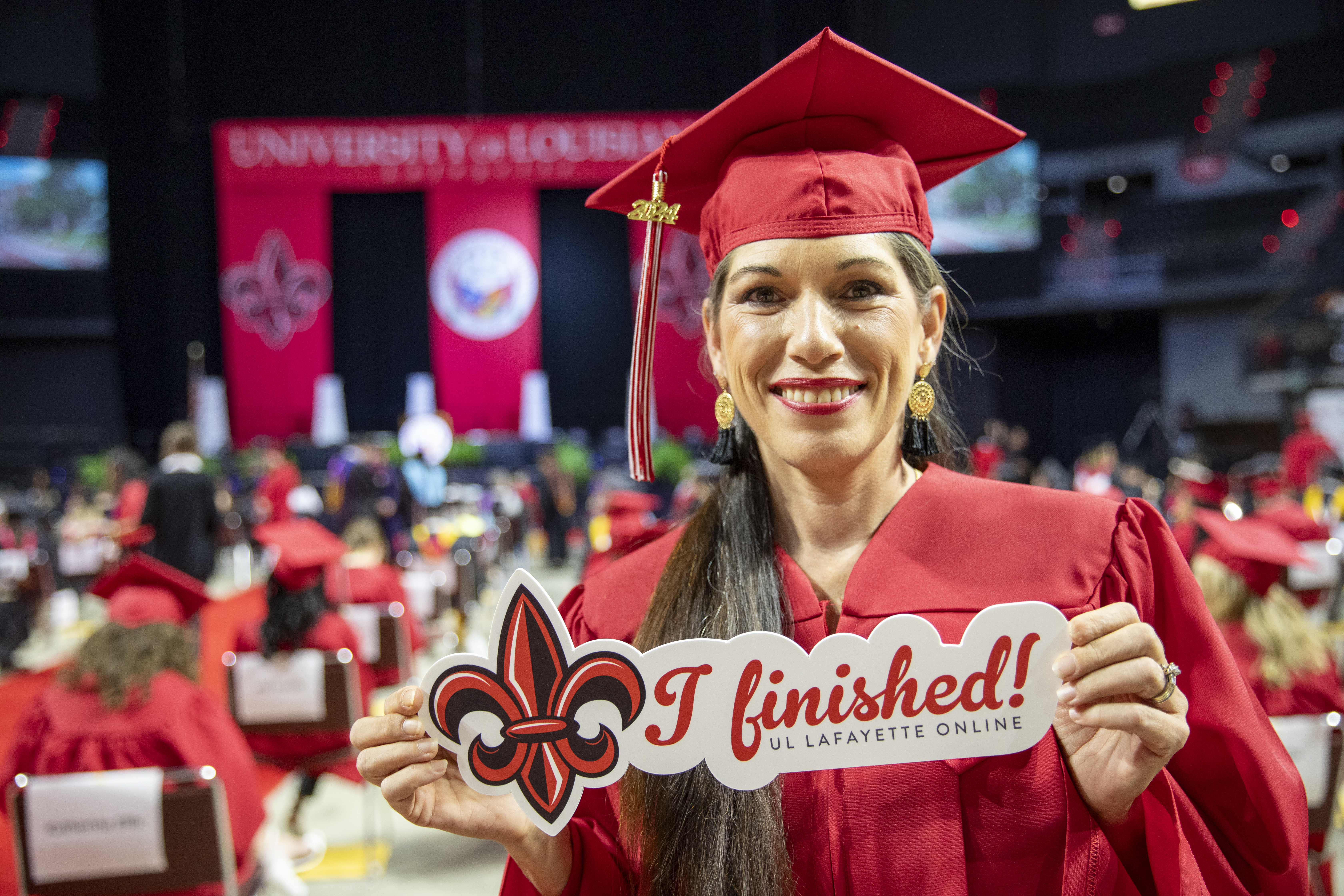 General Studies graduate Bille Mahoney smiles in cap and gown while holding a sign reading "I finished!"