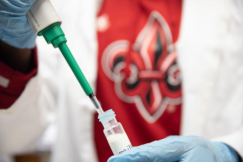 A close-up photo of UL Lafayette researcher using a dropper to put samples in a test tube.