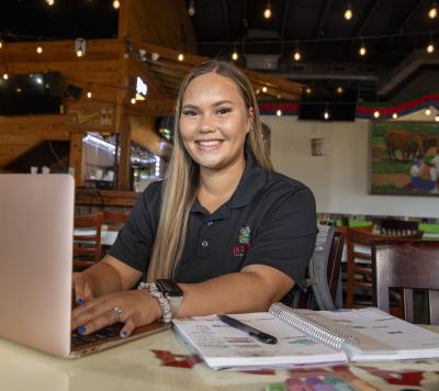 General Studies grad Michele Simon smiles in work uniform while completing an assignment on her laptop