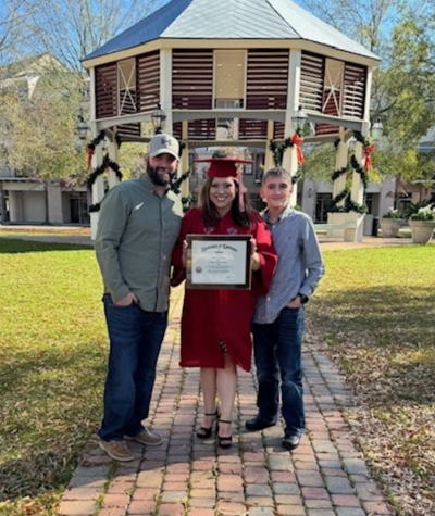 Tiffany Soudelier stands between her husband and son, smiling over her degree on graduation day