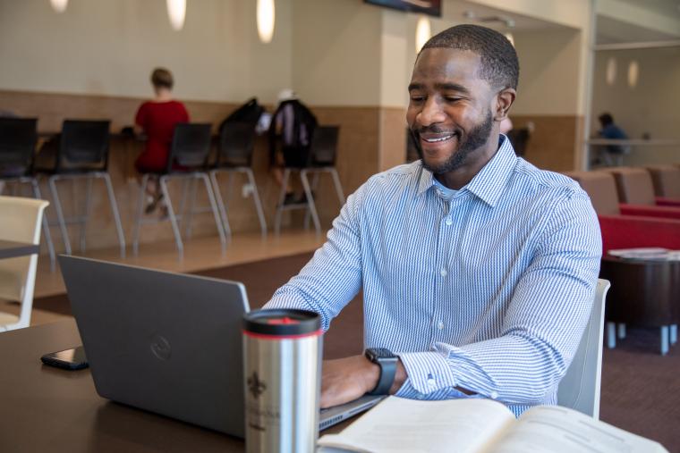 UL Lafayette online MBA student studies on campus wearing a blue collared shirt