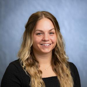 Headshot: Rikki Trahan pictured on a blue/gray background.