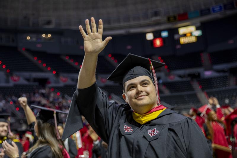 Mason Blanchard, wearing his master's regalia, waves up at his family after having his M.S. in Systems Technology degree conferred.